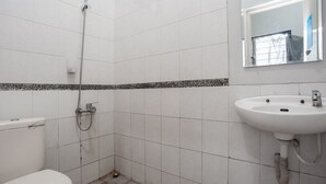 A small, clean bathroom with white tiles, a shower, a toilet, and a sink with a mirror above it. - RedDoorz Syariah near Margonda Raya (Depok)