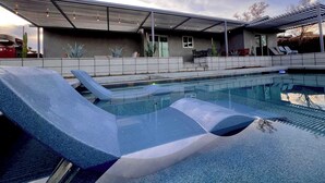 A swimming pool with lounge chairs, a covered patio area, and a view of the sky.