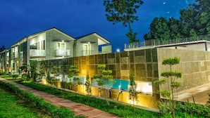 A modern two-story house with a swimming pool, surrounded by well-maintained greenery and a stone wall. - The Cloyster Resort and Spa (Ramnagar)