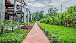 A modern building with a glass facade, a red pathway, and lush greenery. - The Cloyster Resort and Spa (Ramnagar)