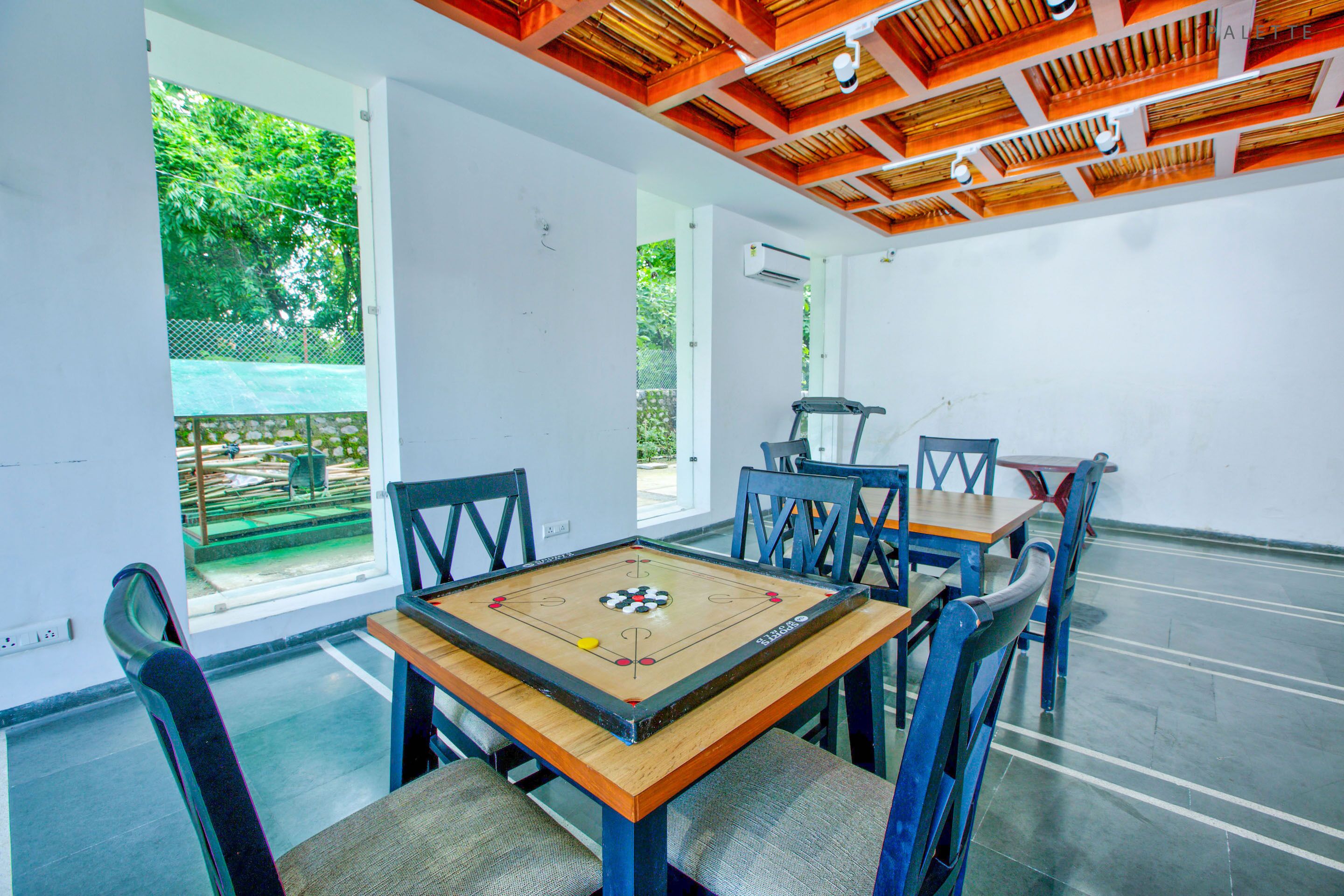 A room with a wooden table and chairs, a window with a view of greenery, and a ceiling with wooden beams.