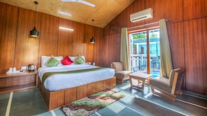 A wooden-paneled room with a bed, a chair, a table, and a ceiling fan. - The Cloyster Resort and Spa (Ramnagar)
