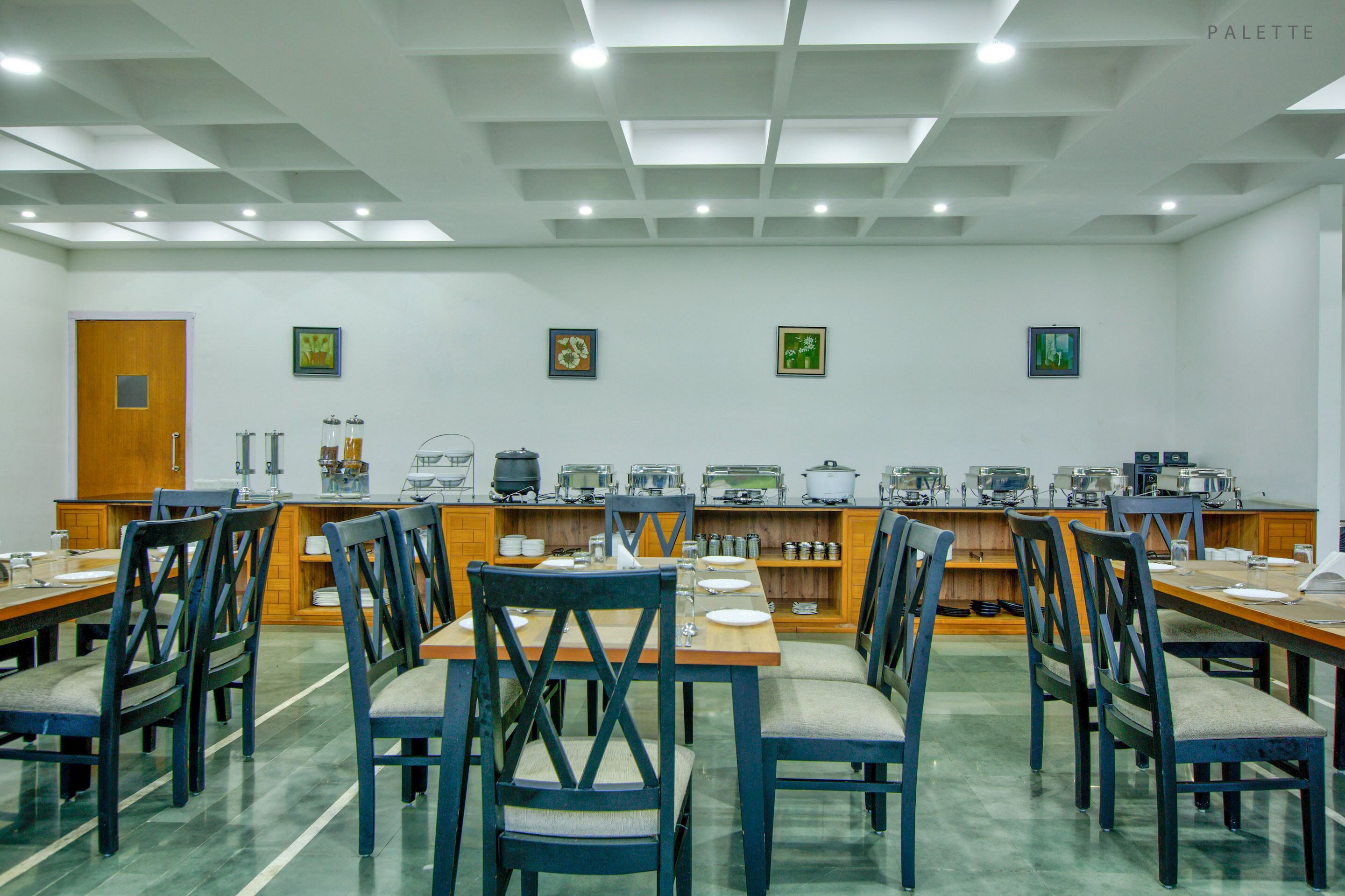 A dining area with multiple tables and chairs, a kitchen area with appliances, and framed artwork on the walls.