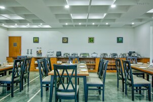 Un comedor con varias mesas y sillas, una zona de cocina con electrodomésticos y cuadros en las paredes.