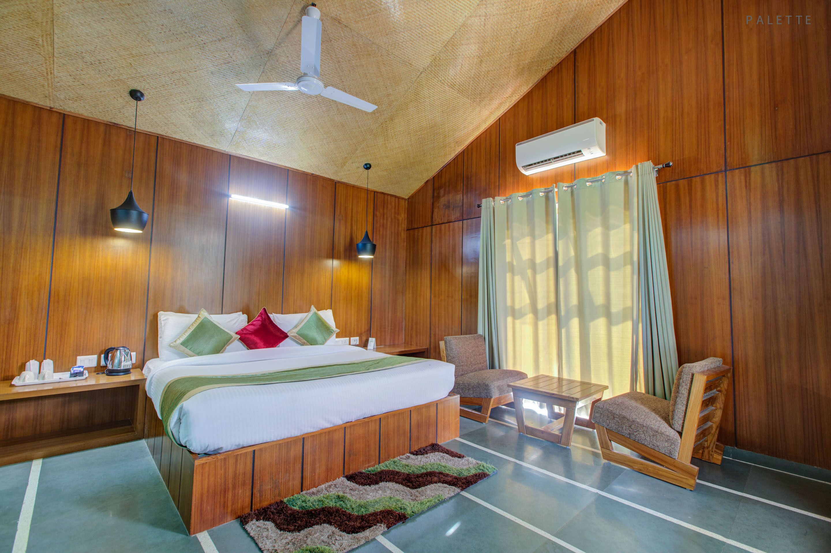Una habitación con paneles de madera, una cama, una silla, una mesa y un ventilador de techo.