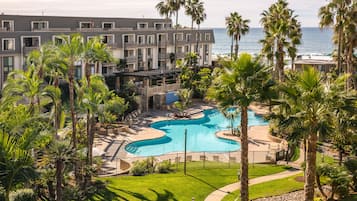 A resort with a swimming pool, palm trees, and a view of the ocean.