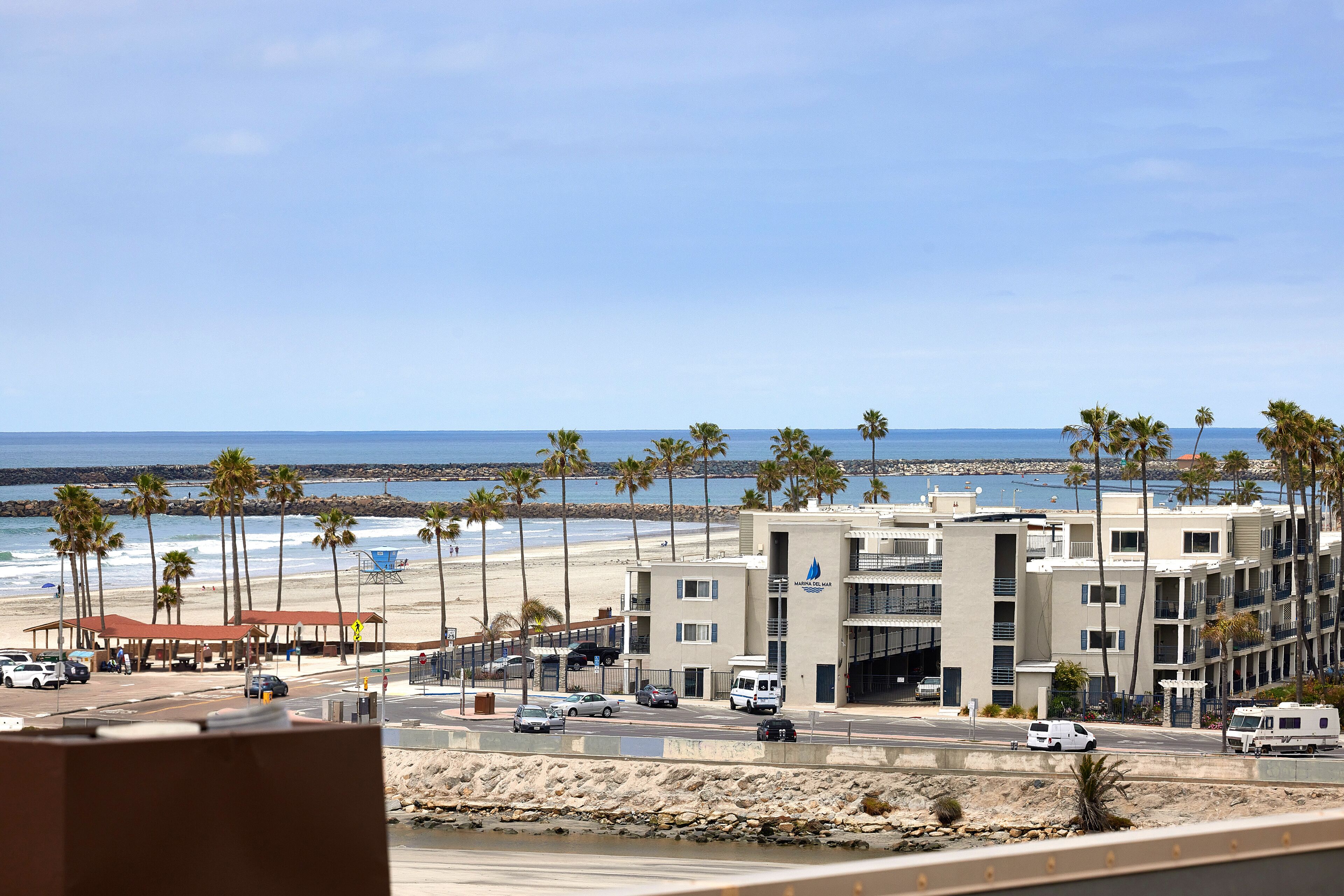 A coastal hotel with a beach view, multiple floors, and a parking area with several vehicles.