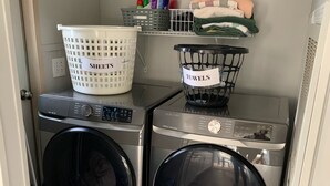 A laundry area with two front-loading washing machines, a basket labeled "SHEETS," and a basket labeled "TOWELS." - Cardinal  Cottage 55 Patton Cemetery Road (Swannanoa)