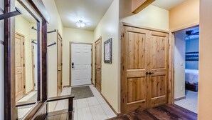 Un corridoio con porte in legno, una porta bianca in fondo e un letto nella stanza adiacente.