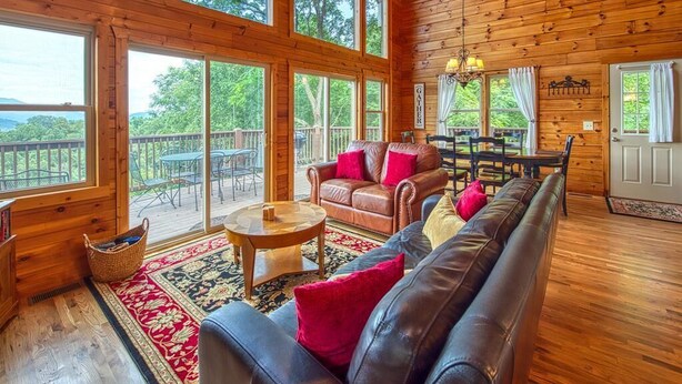 Une cabane en bois spacieuse, dotée de grandes fenêtres, d’un canapé en cuir, d’une table à manger et offrant une vue sur l’extérieur.