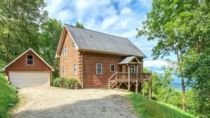 Une cabane en rondins avec une allée en gravier et une jetée qui s’avance dans un lac.