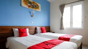 A hotel room with two beds, a blue wall, a painting, and a window with curtains.
