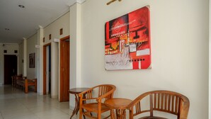 A hotel lobby with wooden chairs and tables, a large abstract painting on the wall, and a tiled floor.