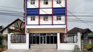A multi-story building with a white facade, blue and red trim, and a gated entrance. - Reddoorz @ Sindangbarang Bogor (Bogor)