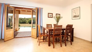 A dining area with a wooden table and chairs, a view of a swimming pool, and framed pictures on the wall. - Can MARES. Stunning villa. A great choice (Pollensa)