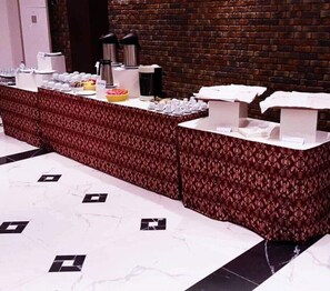 A reception area with a brick wall and marble flooring. There are two reception counters with coffee machines and a basket of pastries. - Hotel Capitol Abidjan (Abidjan)