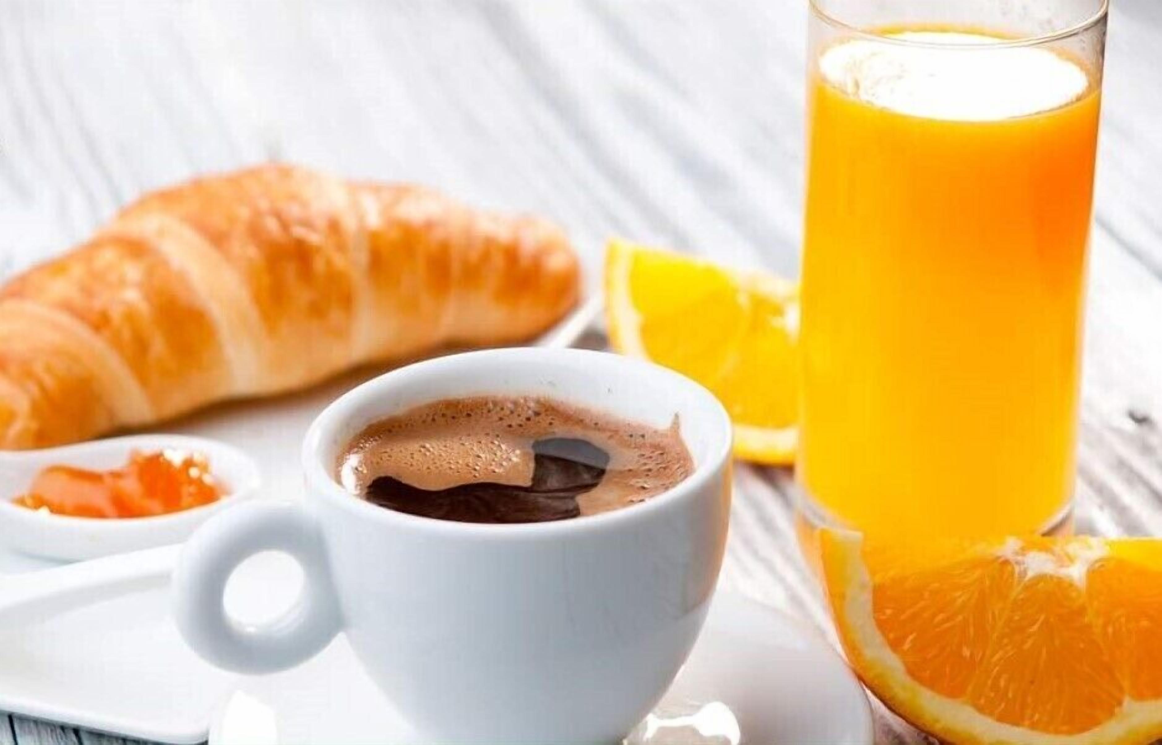 A croissant, a cup of coffee, and a glass of orange juice on a white plate.