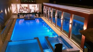 A swimming pool with a tiled deck and a bar area with glass doors.