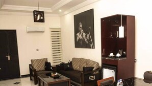 A modern living room with a sofa, two coffee tables, a dining table with chairs, a dark wooden cabinet, and a black and white patterned wall hanging.