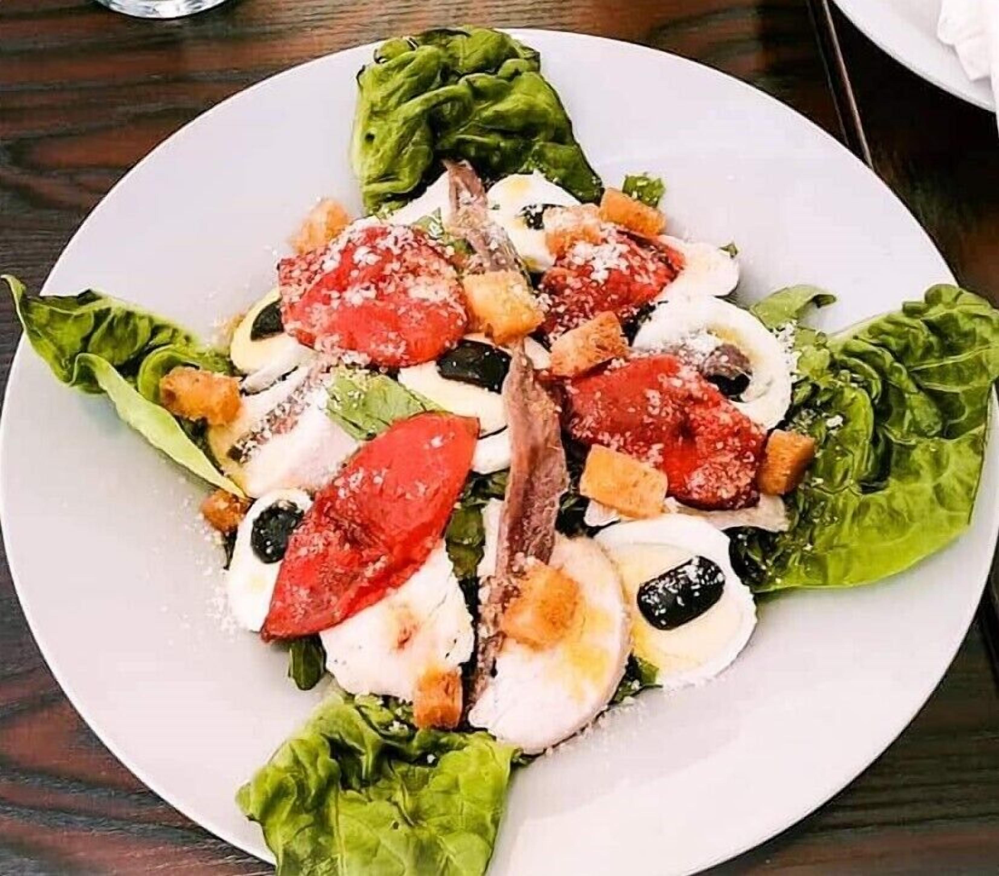 A plate of Caprese salad with tomatoes, mozzarella, and basil on a white plate.