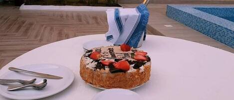 Una mesa de postres con pastel, champán y platos, ubicada al aire libre cerca de una piscina.