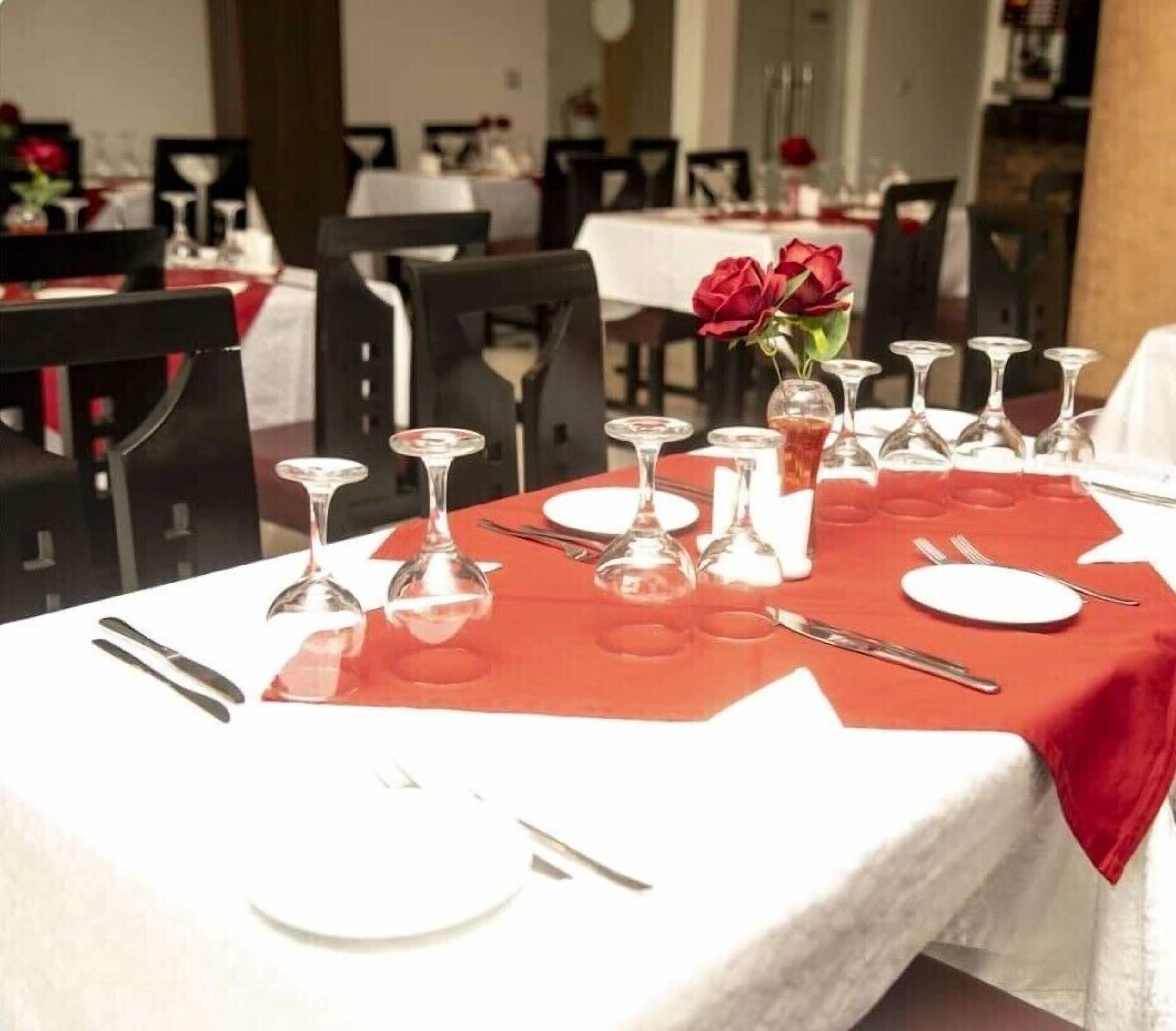 Une table à manger dressée avec une nappe rouge, des assiettes blanches et des verres à vin transparents.