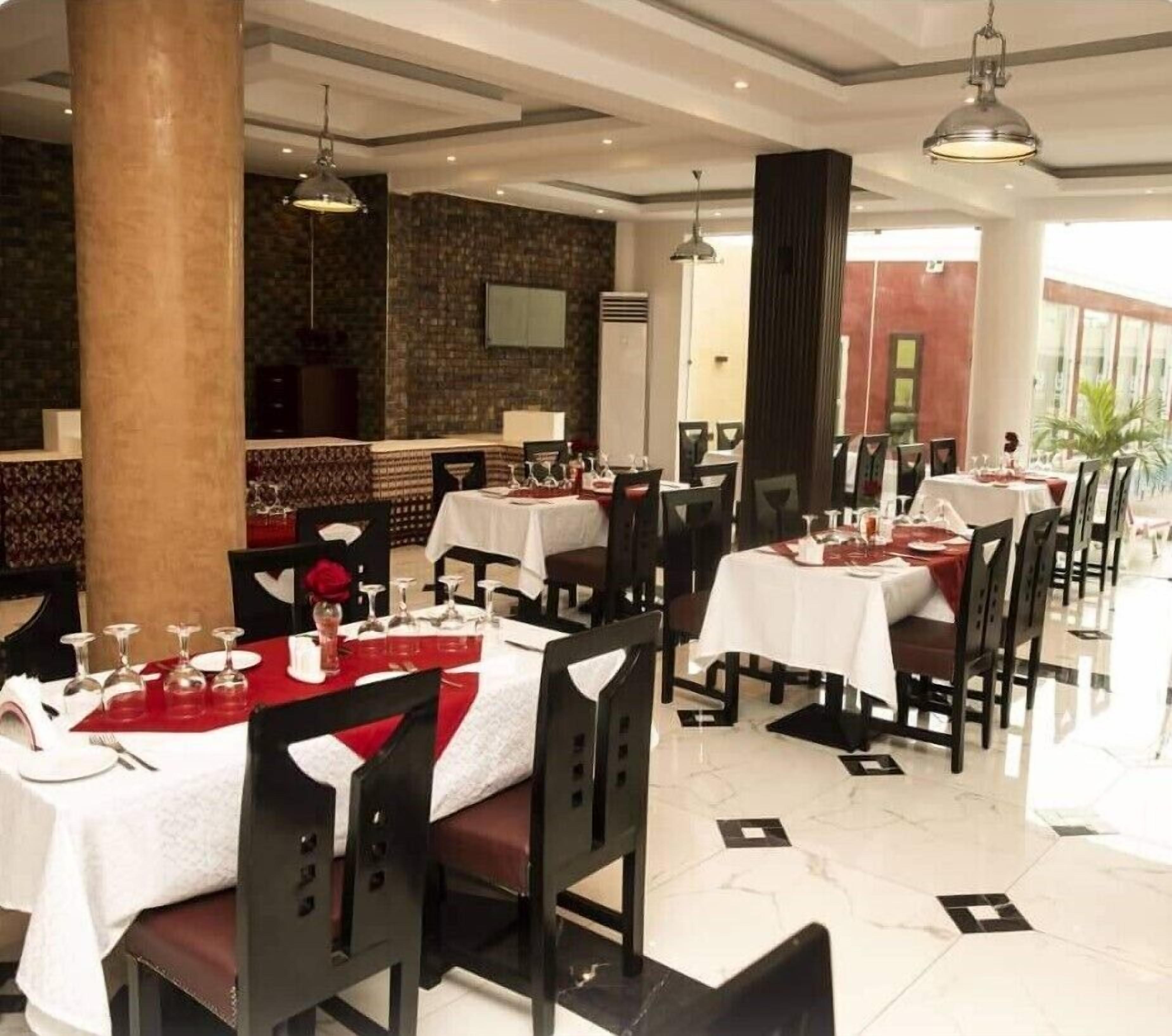 A restaurant with multiple tables set for dining, featuring a modern interior with a stone wall and large columns.