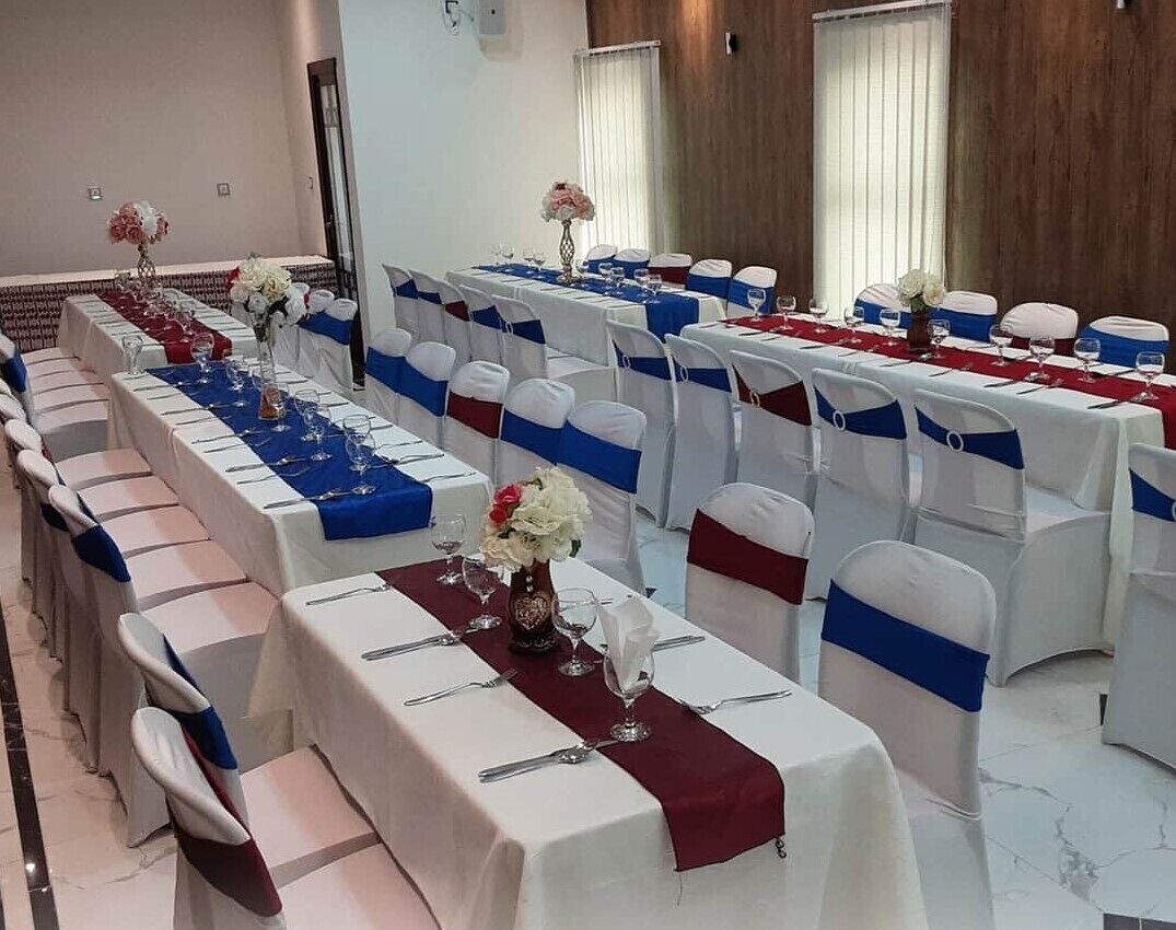 A banquet hall with long tables set for a formal event, featuring white tablecloths, blue and red sashes, and floral centerpieces.