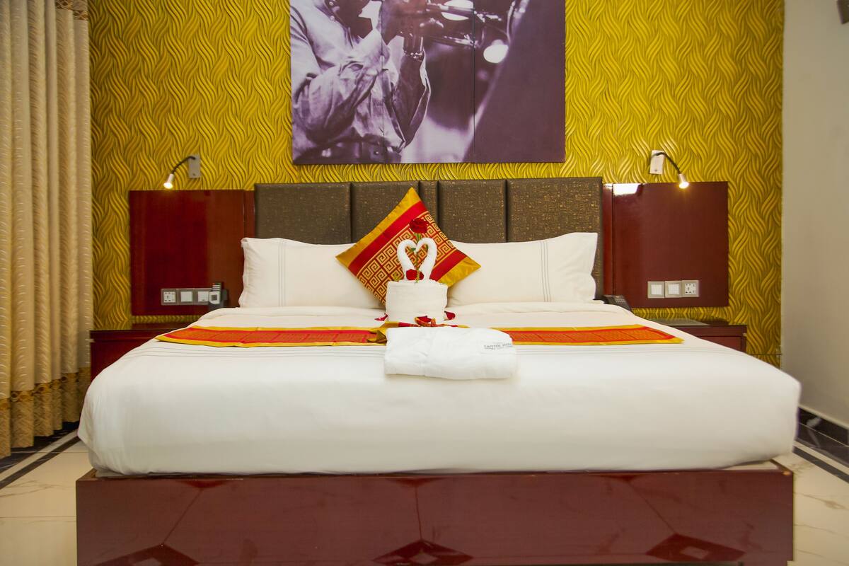 A hotel room with a large bed, two bedside tables, a headboard, and a wall with a patterned wallpaper.