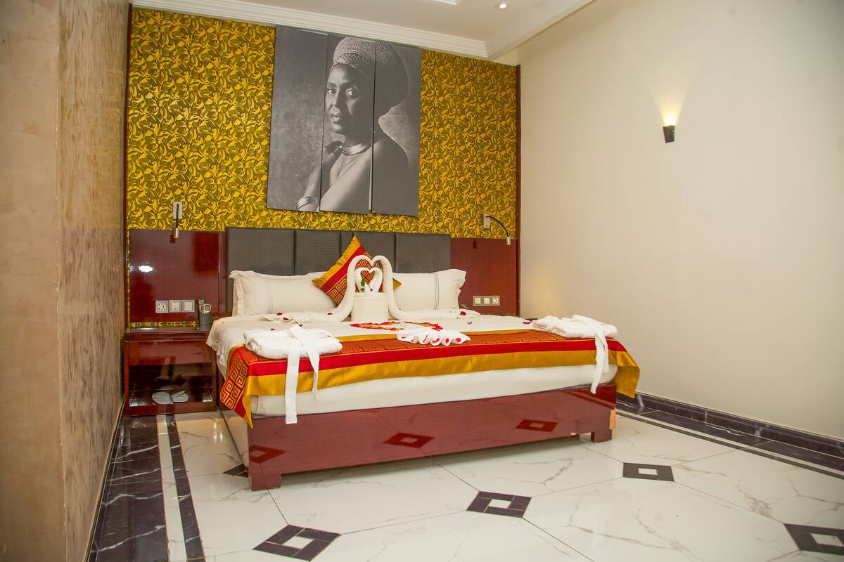 A hotel bedroom with a large bed, a headboard with a decorative panel, a nightstand, and a wall-mounted light.
