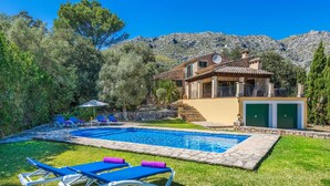 A pool with lounge chairs, a stone pathway, and a building with a green door. - TOMAS. Pretty and classical  villa close to Cala San Vicente (Cala San Vicente)