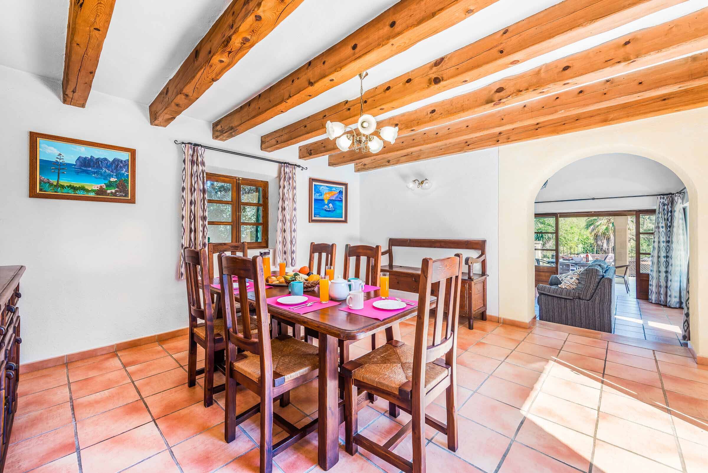 Un espace repas avec des meubles en bois, un sol carrelé et une vue sur un espace extérieur aménagé en salon, accessible par une arche.