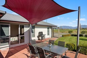A patio with a table and chairs, a barbecue grill, and a large shade sail. - Paradise in Pohara - Pohara Beach Holiday Home (Pohara Beach)