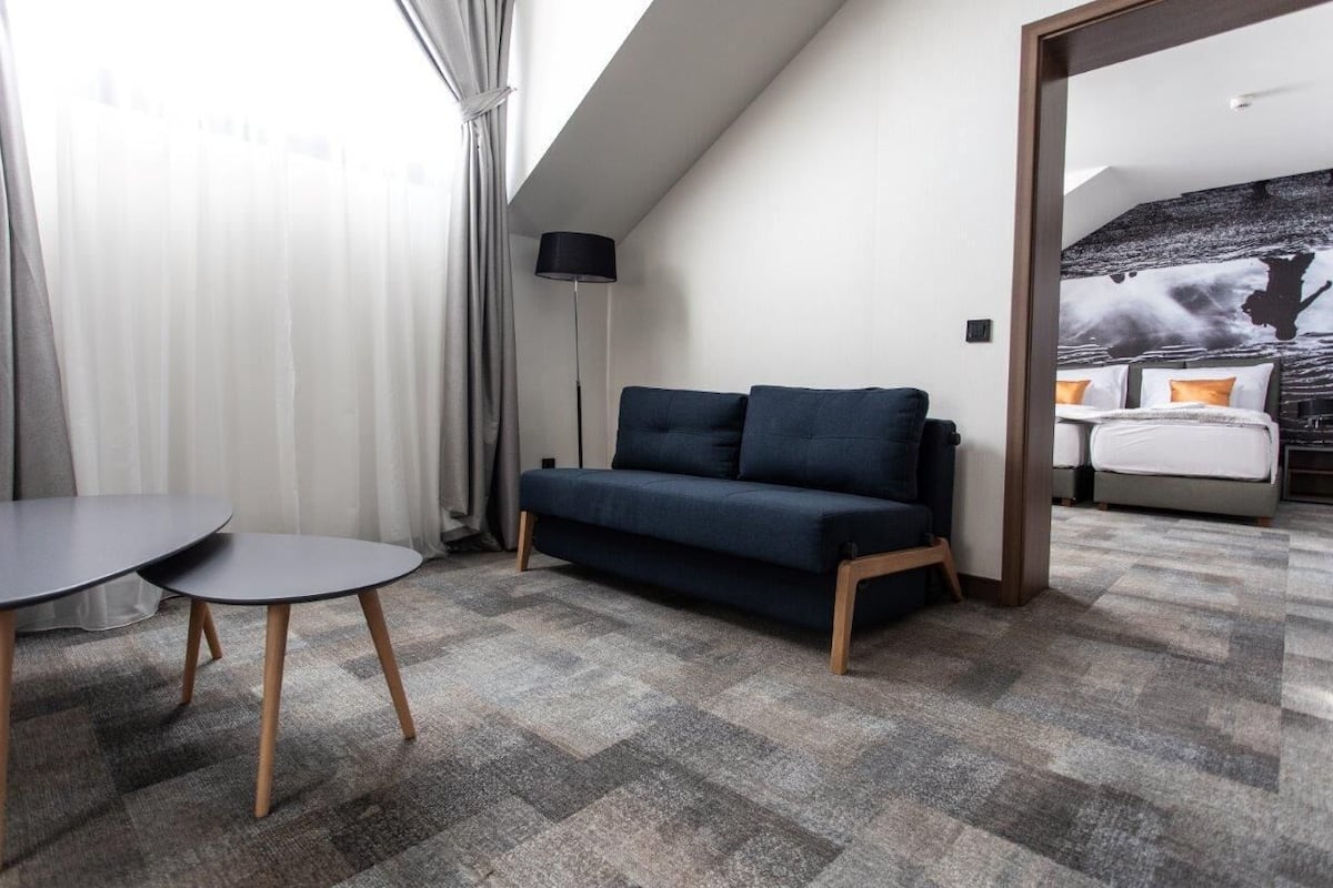 Una habitación de hotel moderna con un sofá, una mesita y una cama con un mural en la pared.
