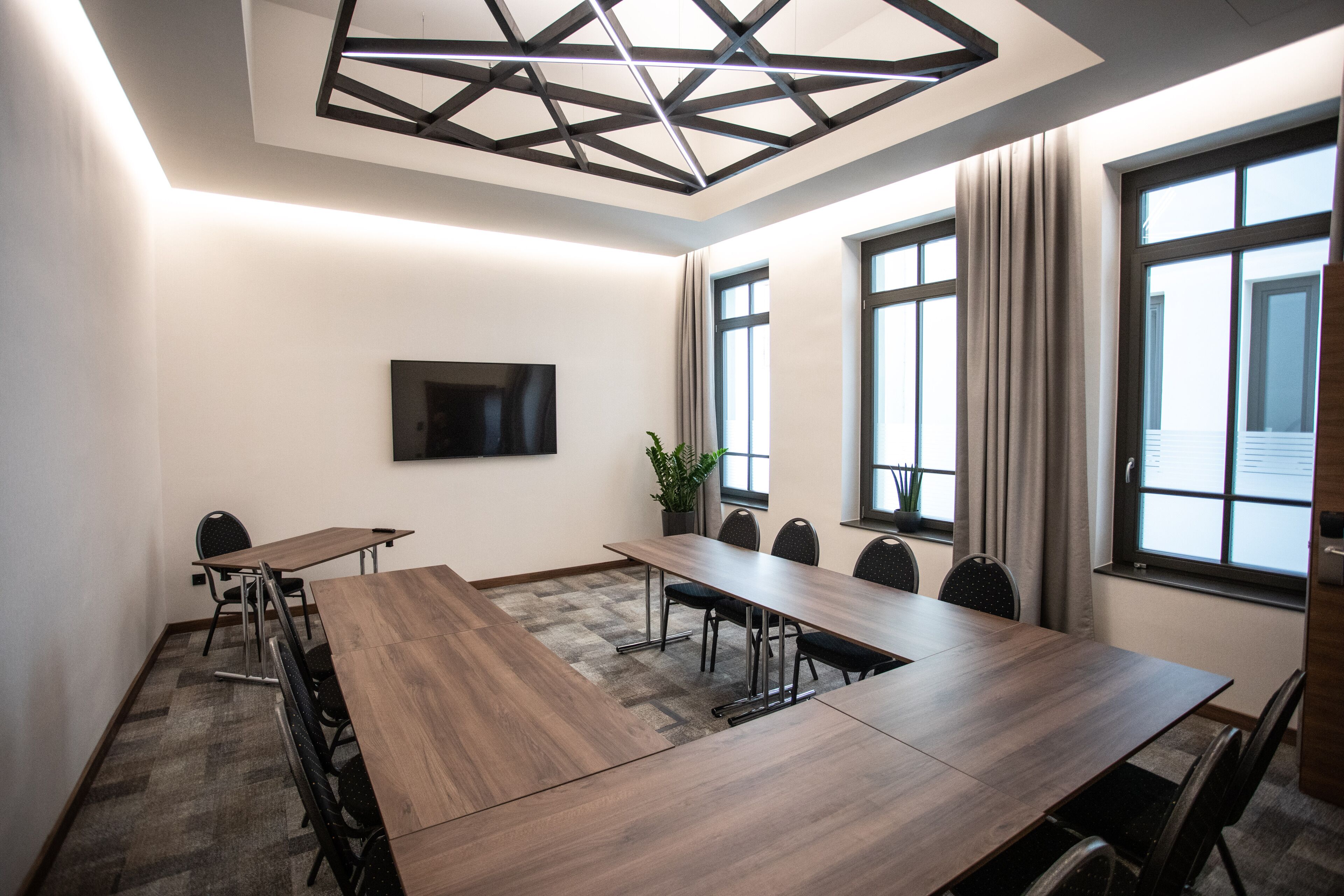 Une salle de conférence équipée d’une longue table, de chaises, d’un téléviseur à écran plat et de grandes fenêtres avec des rideaux.