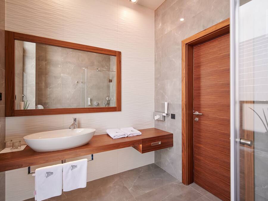 A modern bathroom with a large mirror, a wooden vanity, a sink, and a glass shower enclosure.