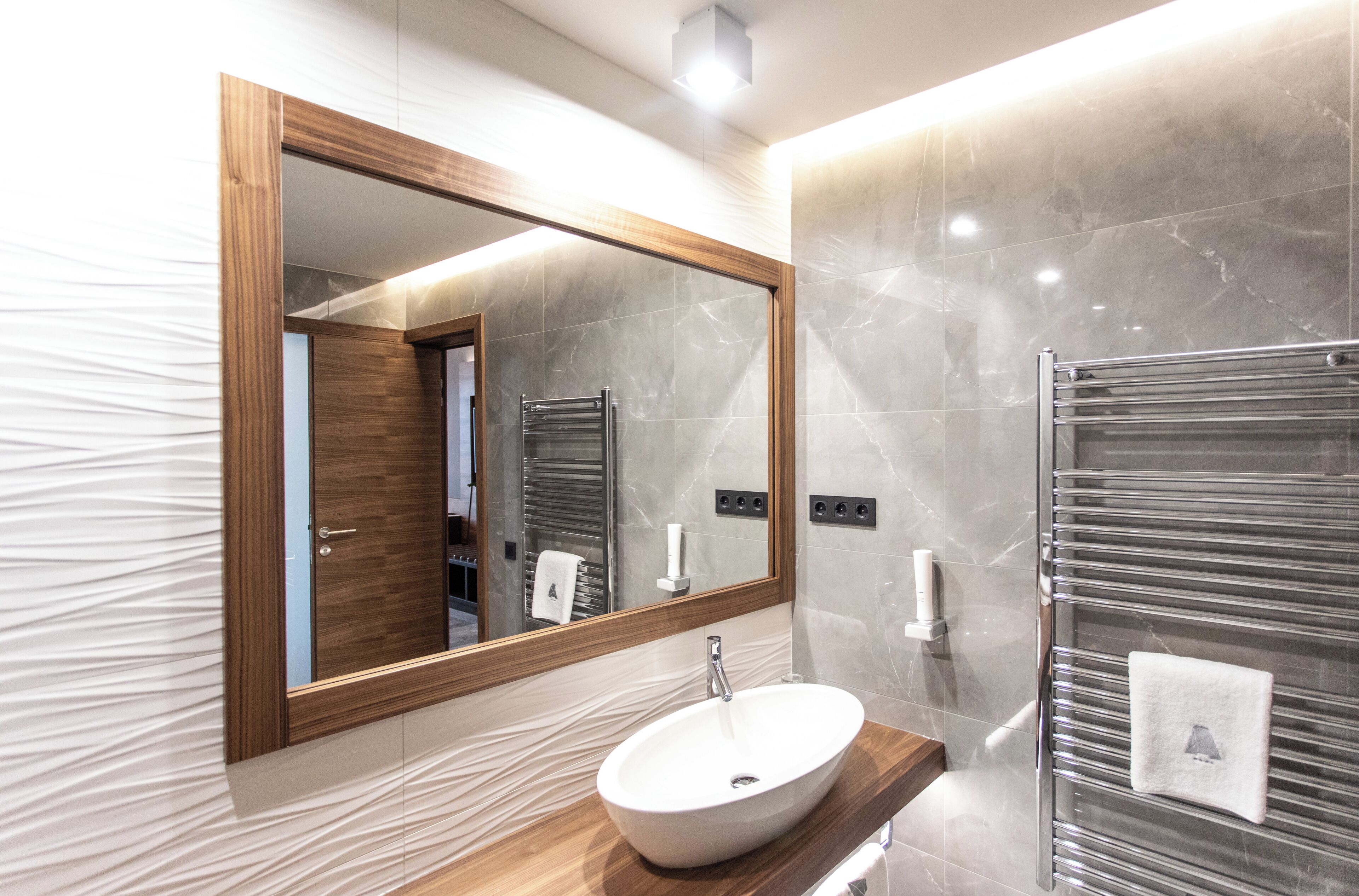 A modern bathroom with a wooden vanity, a large mirror, a white sink, and a glass shower enclosure.