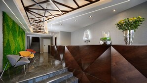Una moderna zona de recepción con una pared verde, escaleras de mármol y un mostrador con un logotipo.