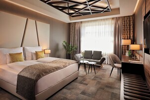 Una habitación de hotel con una cama grande, un sofá, una mesita y un televisor.