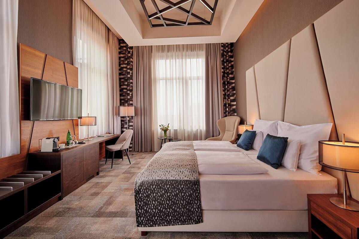 Una habitación de hotel moderna con una cama grande, un escritorio, un televisor y una mesita con una lámpara.