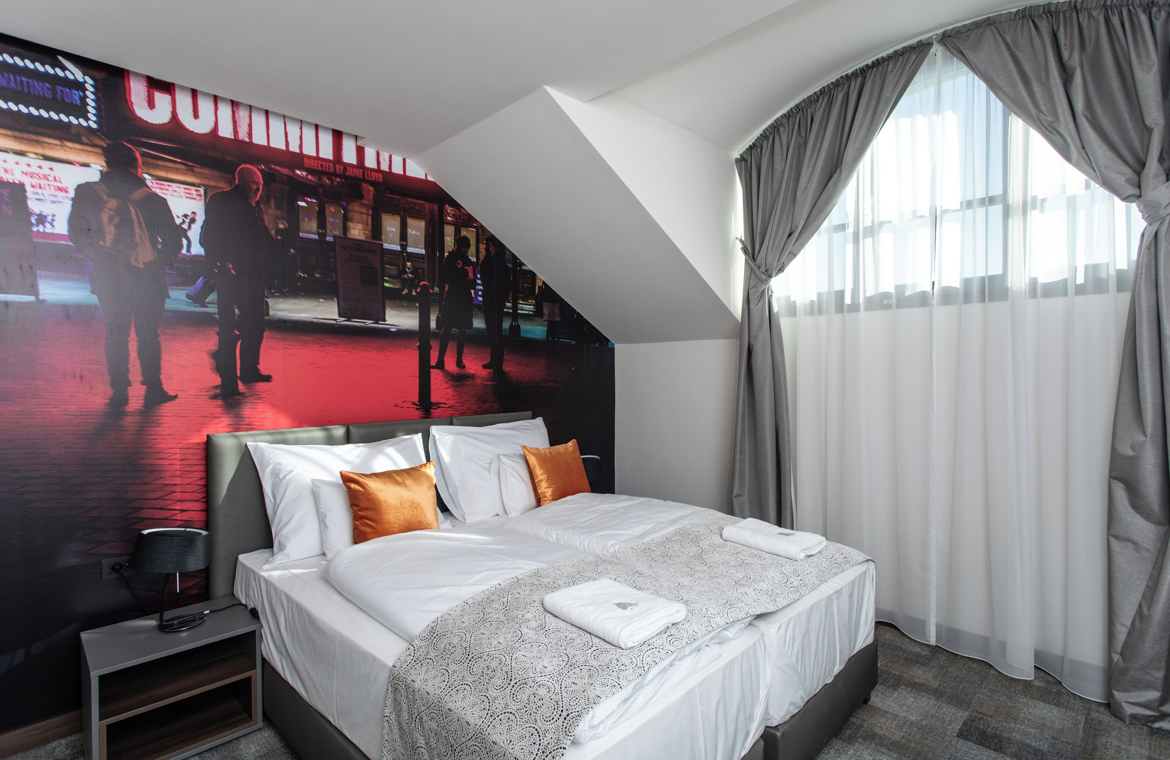 Habitación de hotel con cama, mesita de noche, lámpara y un cartel grande en la pared.