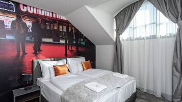 Habitación de hotel con cama, mesita de noche, lámpara y un cartel grande en la pared.