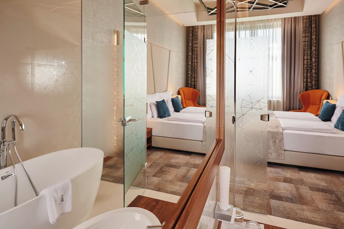 Una habitación de hotel moderna con un espejo grande, una bañera, una cama con almohadas y una ventana con cortinas.