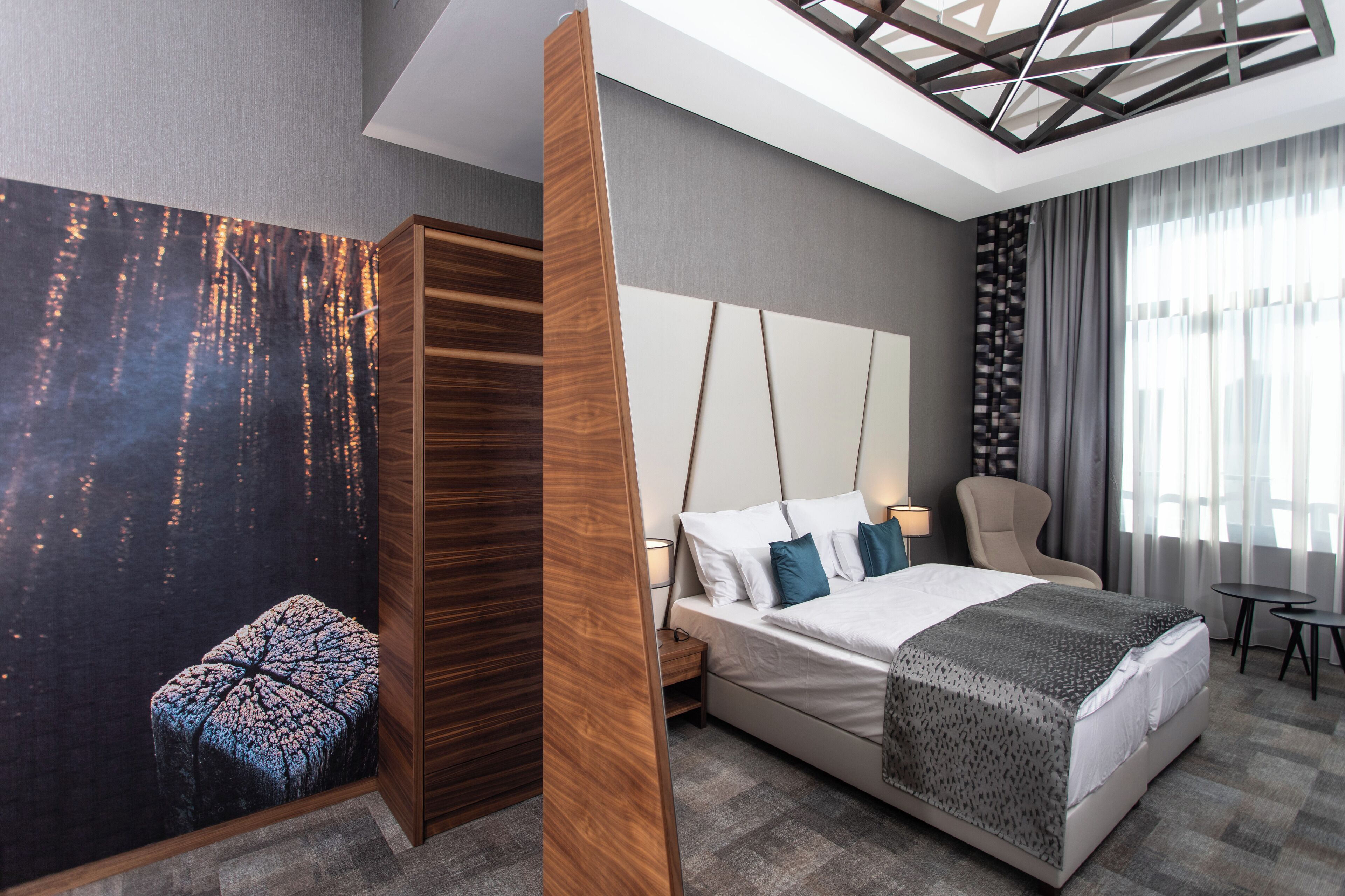 A modern hotel room with a large bed, a wooden wardrobe, a nightstand, a chair, and a small table.