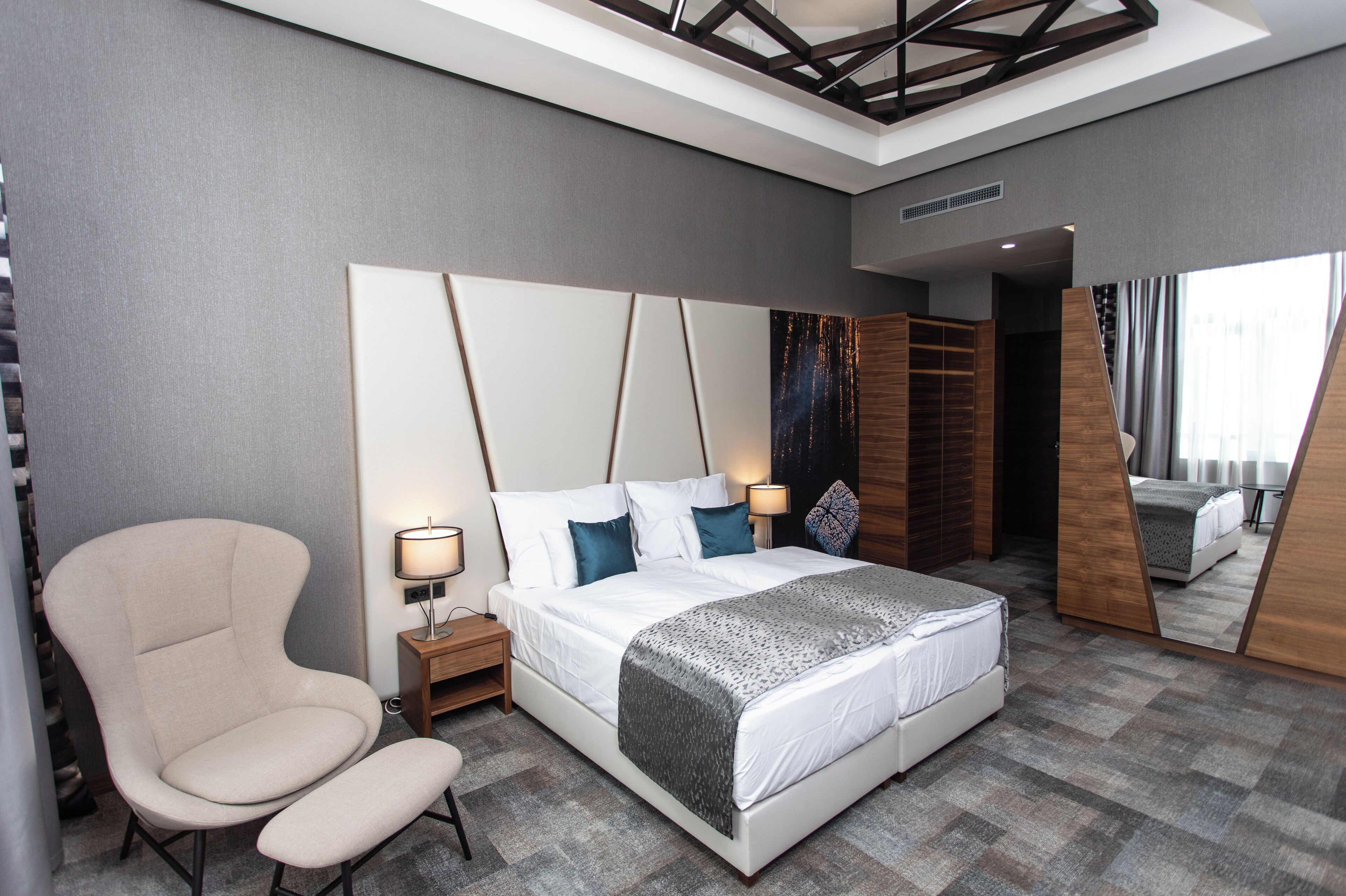 A modern hotel room with a large bed, a chair, a nightstand, and a mirror.