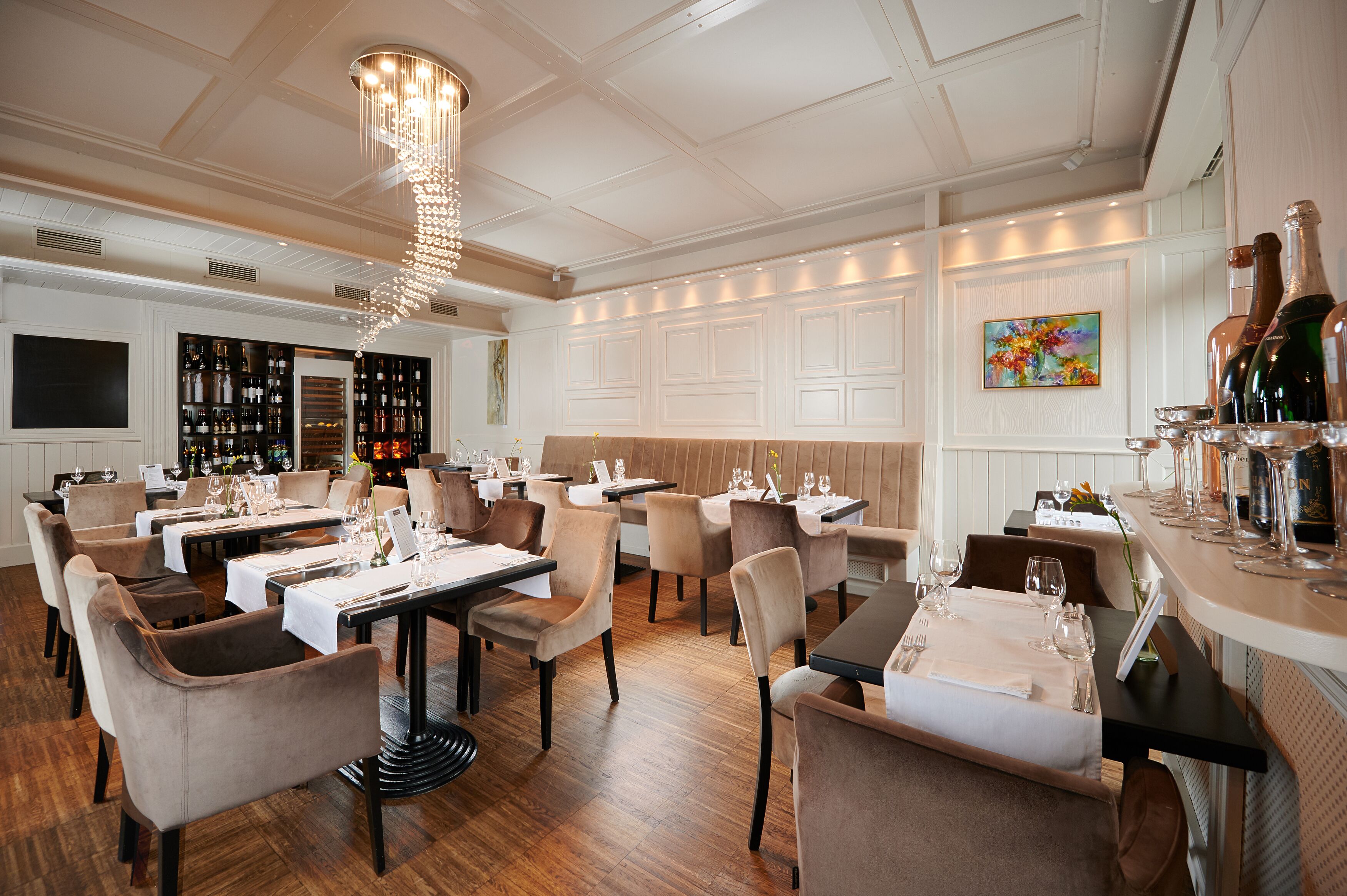 A restaurant with multiple dining tables, chairs, and a bar area with bottles and glasses.