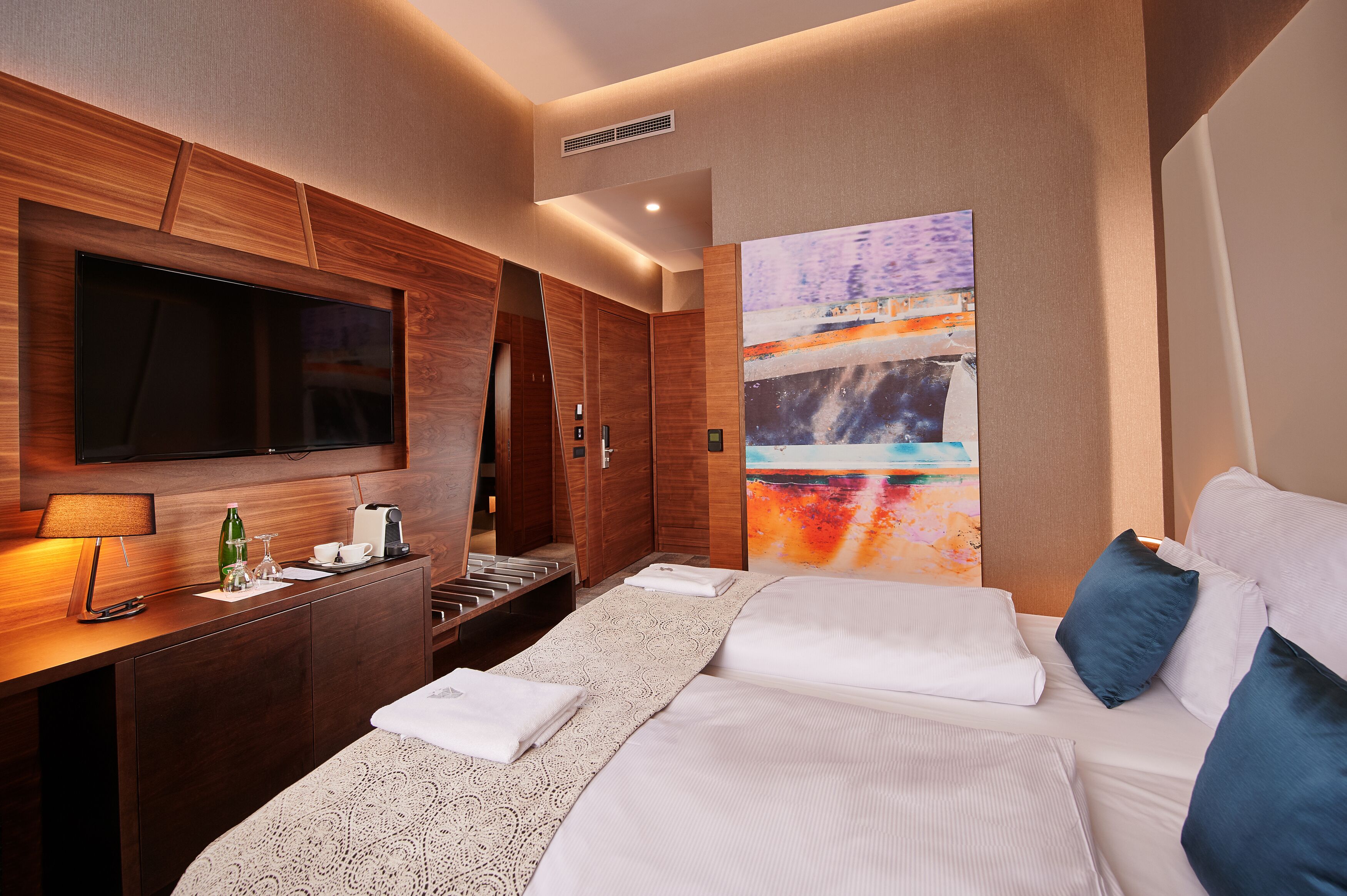 A hotel room with a large bed, a desk with a lamp, a flat-screen TV, and a painting on the wall.