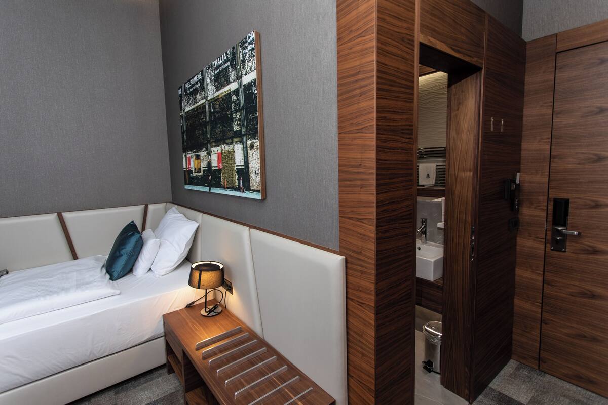 Habitación de hotel moderna con cama, mesita de noche, lámpara y armario de madera.