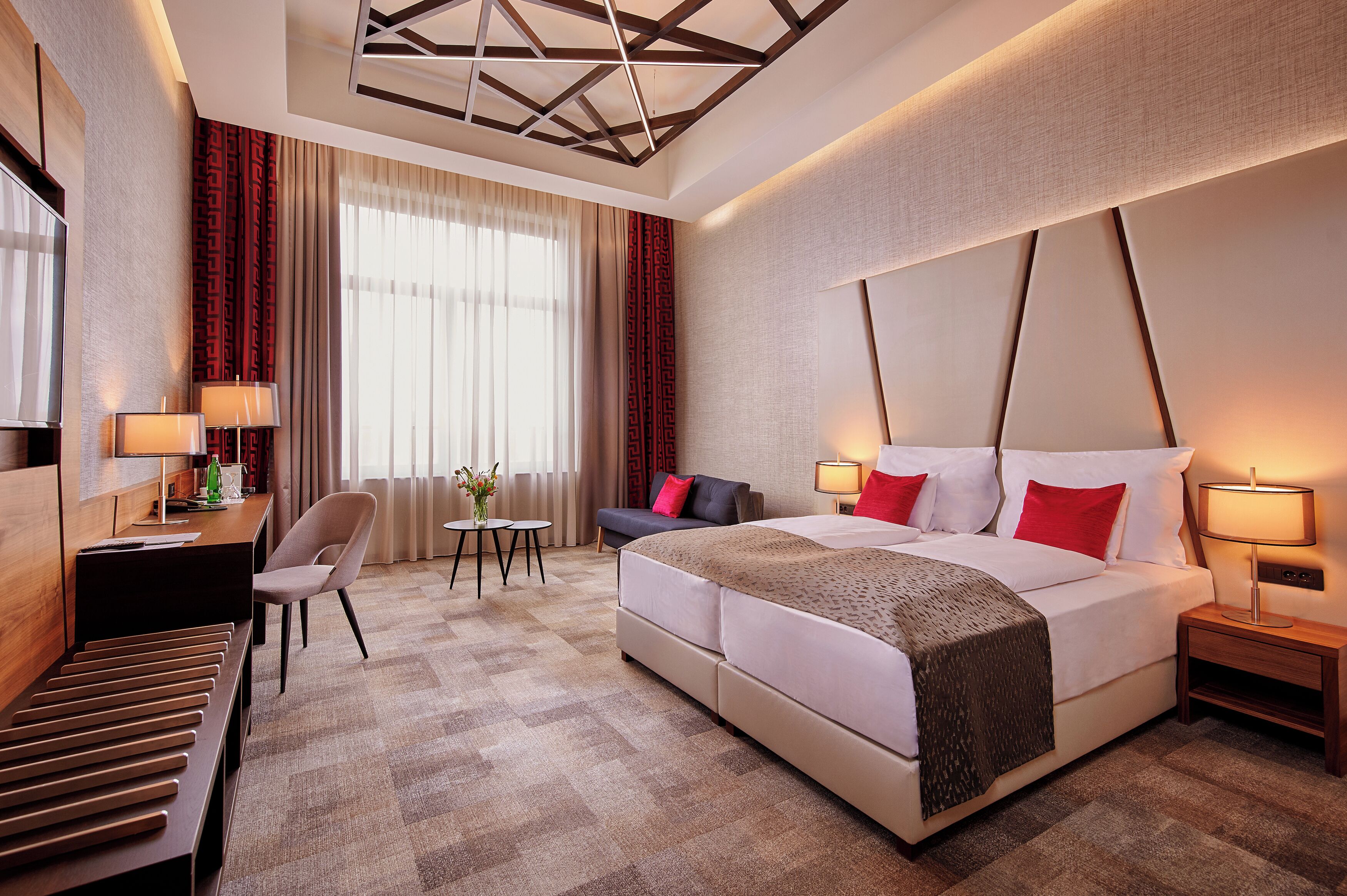 Habitación de hotel con una cama grande, un escritorio con silla, una mesita de noche con lámpara y un sofá.