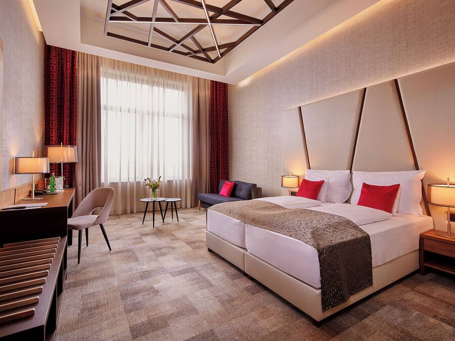 Une chambre d’hôtel avec un grand lit, un bureau avec une chaise, une petite table avec une lampe et un canapé.